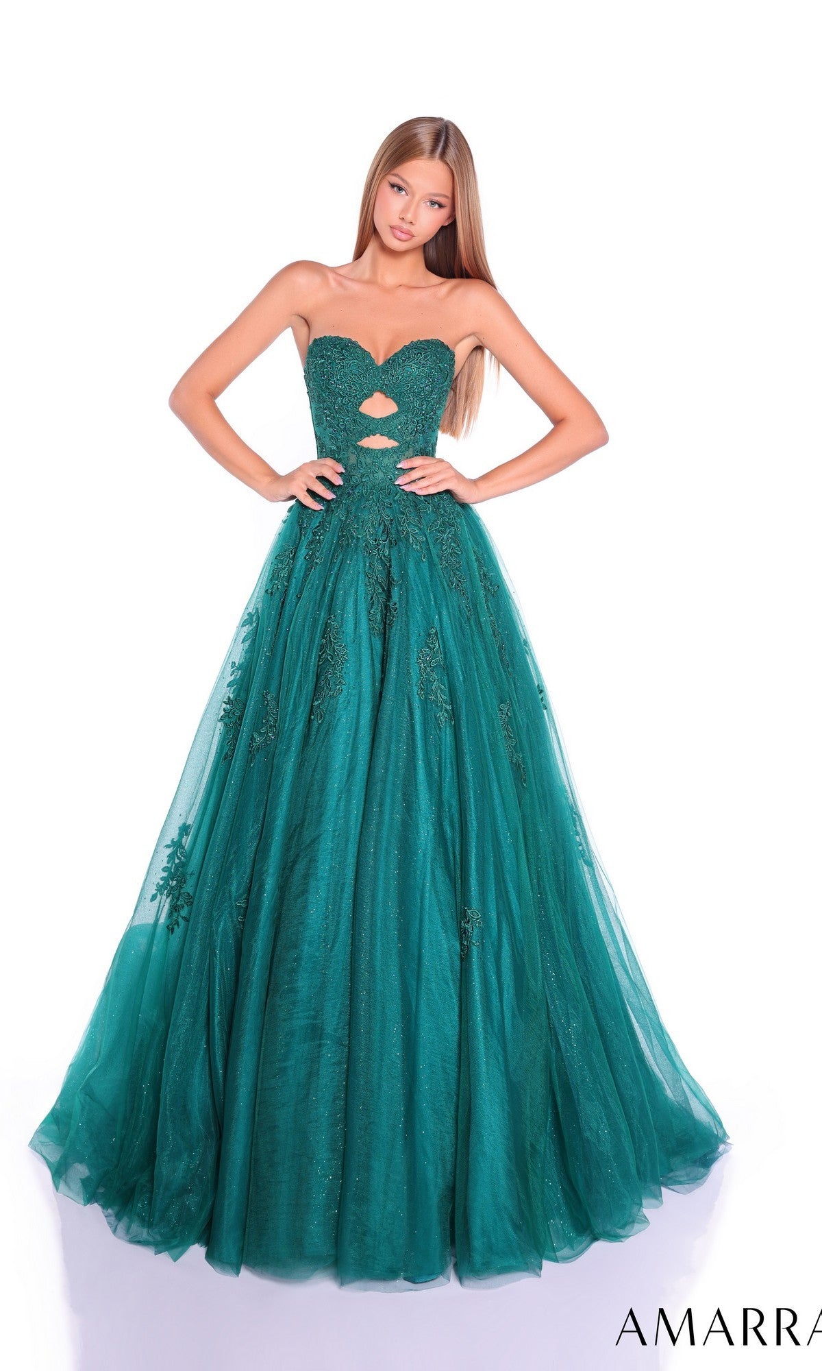 A young woman wears the Amarra 89357 Strapless Cut-Out Long Prom Dress in emerald green, featuring a fitted bodice, cutout details, and a full tulle skirt, posing against a white background.